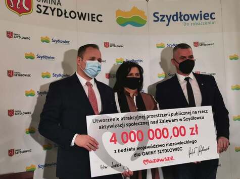 dwóch mężczyzn i jedna kobieta pozują na ściance z czekiem o wartości 4 mln zł 