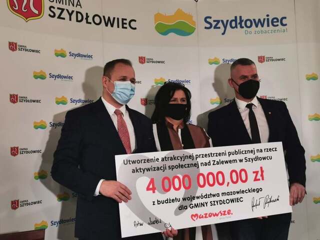 Dwóch mężczyzn i jedna kobieta pozują do zdjęcia z czekiem o wartości 4 mln zł