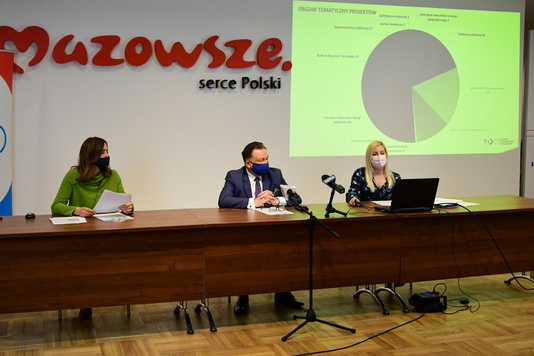 Trzy osoby w maseczkach i z dystansem społecznym za stołem konferencyjnym