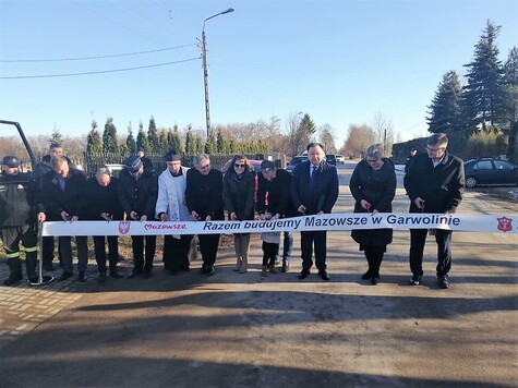 Otwarcie zmodernizowanej drogi. Kilkanaście osób, przedstawicieli mazowieckich samorządów stoi na drodze, przecinając symboliczną wstęgę.