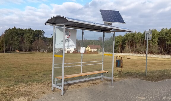 Oszklona wiata przystankowa. Na dachu jest panel słoneczny.