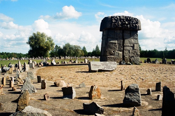 Monumentalny kamień-pomnik, który kołem otaczają drobniejsze kamienie-tablice. Przed monumentem tablica z napisem "nigdy więcej wojny".