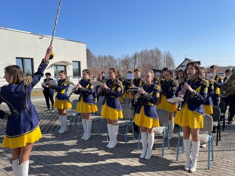 Grupa dziewcząt z zespołu mażionetek ustawiona jest w rzędach. Grają na instrumencie. Dyryguje im dziewczyna w takim samym stroju