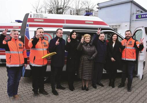 Grupa osób pozuje do zdjęcia na tle karetki pogotowia.