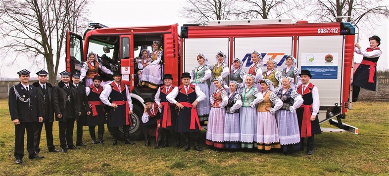 Zespół w strojach ludowych na tle wozu strażackiego