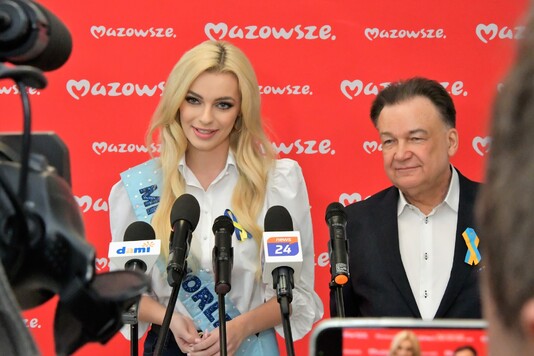 Kobieta i mężczyzna mówią do stojących przed nimi mikrofonów, w tle logo Mazowsza