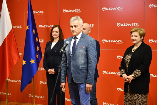 Mężczyzna elegancko ubrany stoi przed mikrofonem.