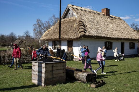 Przed chatą krytą strzechą zwiedzający polewają się z drewnianych sikawek