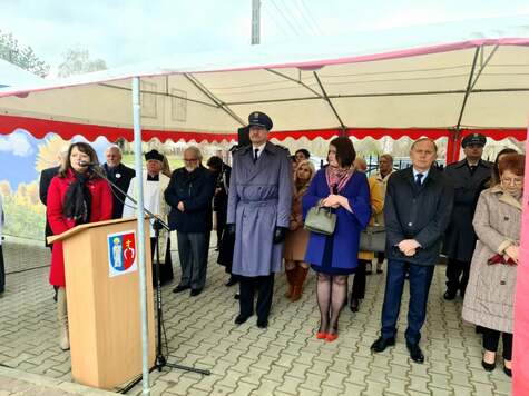 Janina Ewa Orzełowska stoi przy ambonie. Koło niej stoją inni uczestnicy uroczystości  zgromadzeni pod rozstawionym namiotem. 