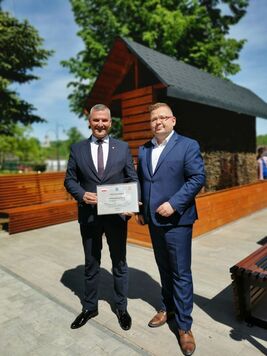 Wicemarszałek trzyma dyplom z podziękowaniami. Obok niego stoi mężczyzna. W tle widać tężnię