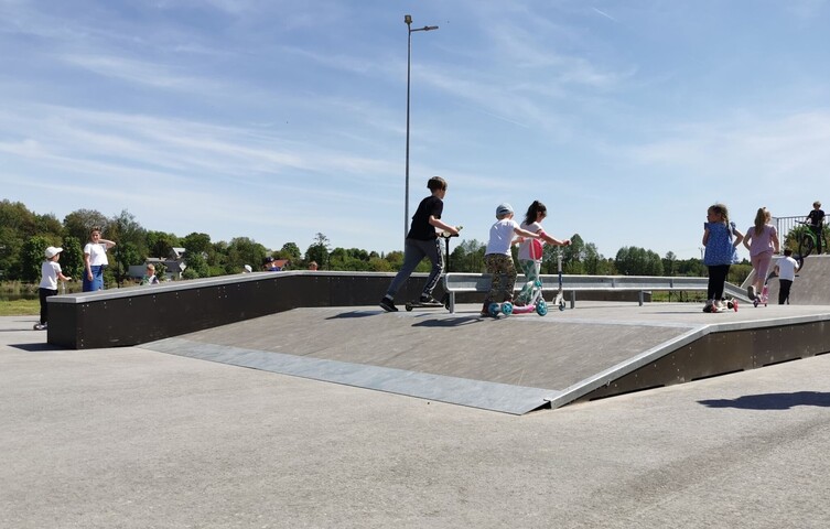 Na betonowej pochylni dzieci jeżdżą na hulajnogach.