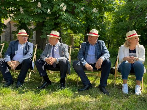 Grupa mężczyzn w słomkowych kapeluszach siedzi na leżakach na łące.