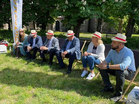 Grupa mężczyzn w słomkowych kapeluszach siedzi na leżakach na łące.