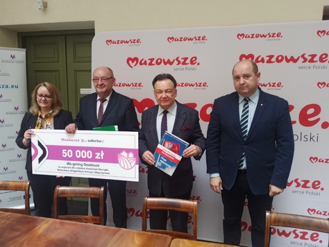 Trzech mężczyzn i jedna kobieta pozują do zdjęcia z czekiem