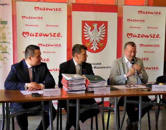 Trzej mężczyźni siedzą za stołem prezydialnym