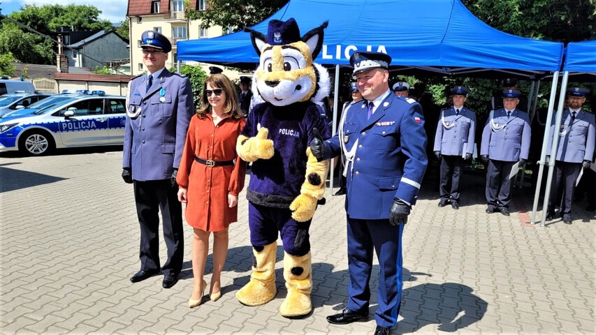 Janina Ewa Orzełowska stoi obok dwóch funkcjonariuszy w galowych mundurach. Między nimi jest trzeci mężczyzna w przebraniu maskotki policji - pluszowego tygrysa w policyjnym mundurze.