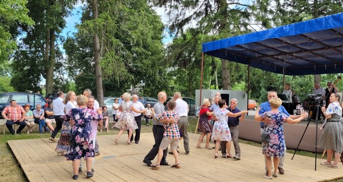 Seniorzy tarczą na wykonanym z desek parkiecie, przed sceną muzyczną