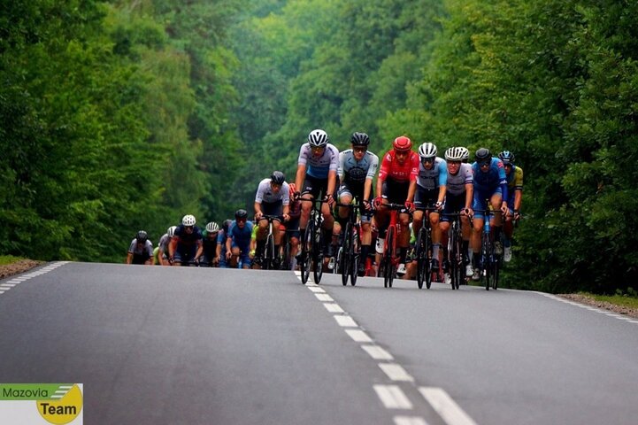 Peleton kolarzy jadący asfaltową drogą przez las. Na czele widać zawodnika Mazowsze Serce Polski