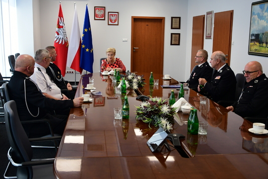 Grupa osób, część w mundurach strażackich, siedzi przy stole i rozmawia.