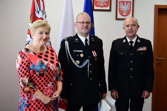 Grupa osób, część w mundurach strażackich, pozuje do zdjęcia.