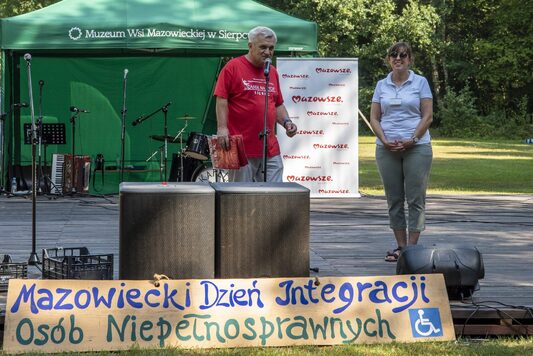 Mężczyzna i kobieta stoja na scenie. Za nimi widać namiot stoiska