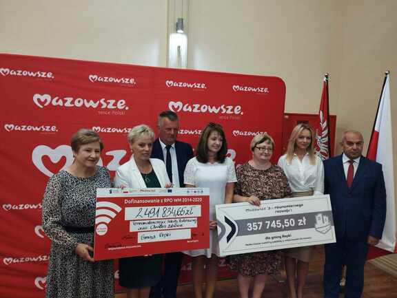 Na zdjęciu 5 kobiet i dwóch mężczyzn pozują do zdjęcia z dwoma czekami