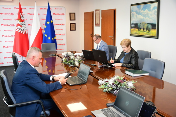 Trzy osoby z zarządu województwa mazowieckiego: Rafał Rajkowski, Elżbieta Lanc, Wiesław Raboszuk siedzą przy stole podczas zdalnego posiedzenia sejmiku.