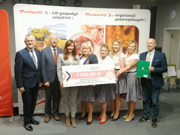 Radni Anna Brzezińska, Piotr Kandyba oraz Stefan Traczyk pozują do zdjęcia z beneficjentami jednego z projektów. Trzymają przed sobą symboliczny czek