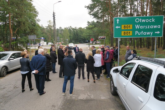 Grupa wielu osób stoi na drodze. W tle widać drogę wojewódzką nr 801.