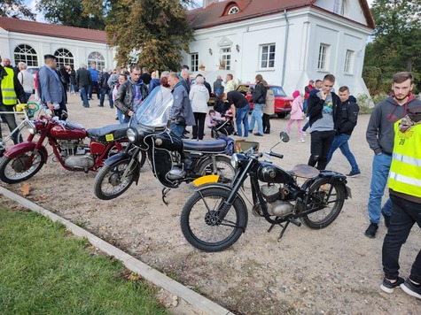 Trzy motocykle stojące na podjeżdzie pałacowym. W tle widać oglądających je ludzi i zabudowania pałacu