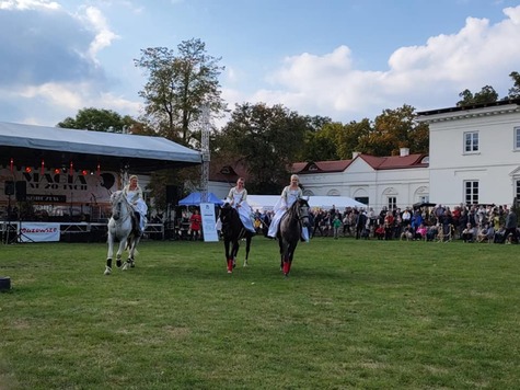 Trzech jeźdźców jedzie na koniach. Ubrani są w dawne tradycyjne stroje. W tle widać obserwujących widowisko ludzi