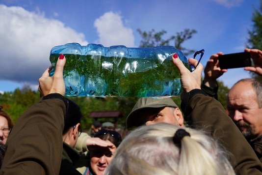 Jeden z uczestników konferencji prezentuje plastikową butlę, w której są młode raki, przygotowane do wypuszeczenia do zbiornika