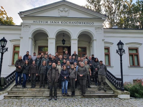 Grupa ludzi pozuje do zdjęcia. Stoją na schodach dworku w Czarnolesie