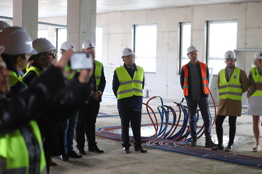 Grupa osób w ubraniach ochronnych i kaskach zwiedza wnętrze budowanego budynku.