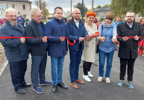 Grupa ustawionych w linię osób przecina czerwoną wstęgę.