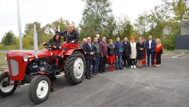 Zabytkowy ciągnik z przyczepą. Za nim ustawiona grupa ludzi.