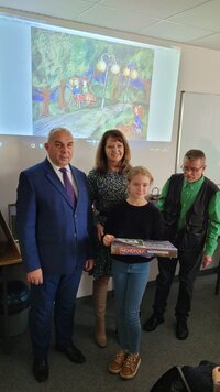 Dyrektor delegatury i Orzełowska pozują do zdjęcia z dziewczynką, która trzyma nagrodę