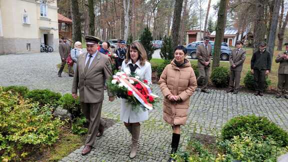 Janina Ewa Orzełowska w towarzystwie dwóch osób składa wieniec