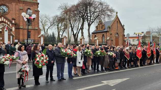 Podczas uroczystości w Łosicach. Delegacje stoją z wieńcami na drodze. W tle kościół.