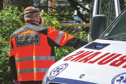 Ratownik medyczny ustawiony tyłem przy karetce.