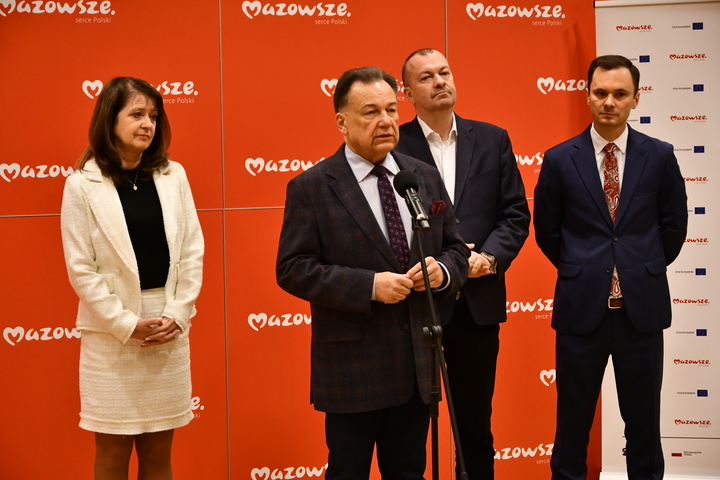 Grupa osób stoi przed mikrofonem podczas konferencji prasowej.