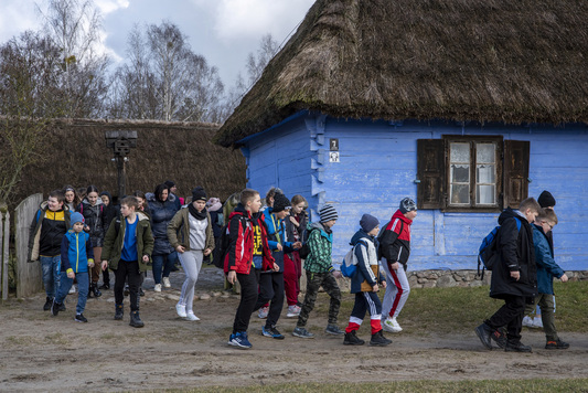 Dzieci idą grupą obok jednej ze skansenowskich chałup