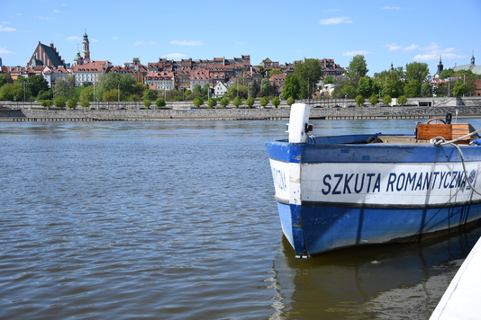 Łódź z napisem sztuka romantyczna. Na drugim brzegu Wisły widać stare miasto