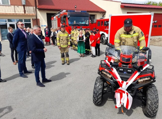 Strażak siedzący na quadzie i inni strażacy oraz samorządowcy