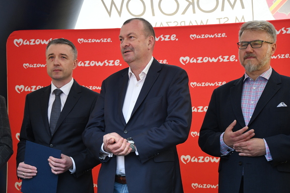 Trzech mężczyzn stoi na tle czerwonej ścianki