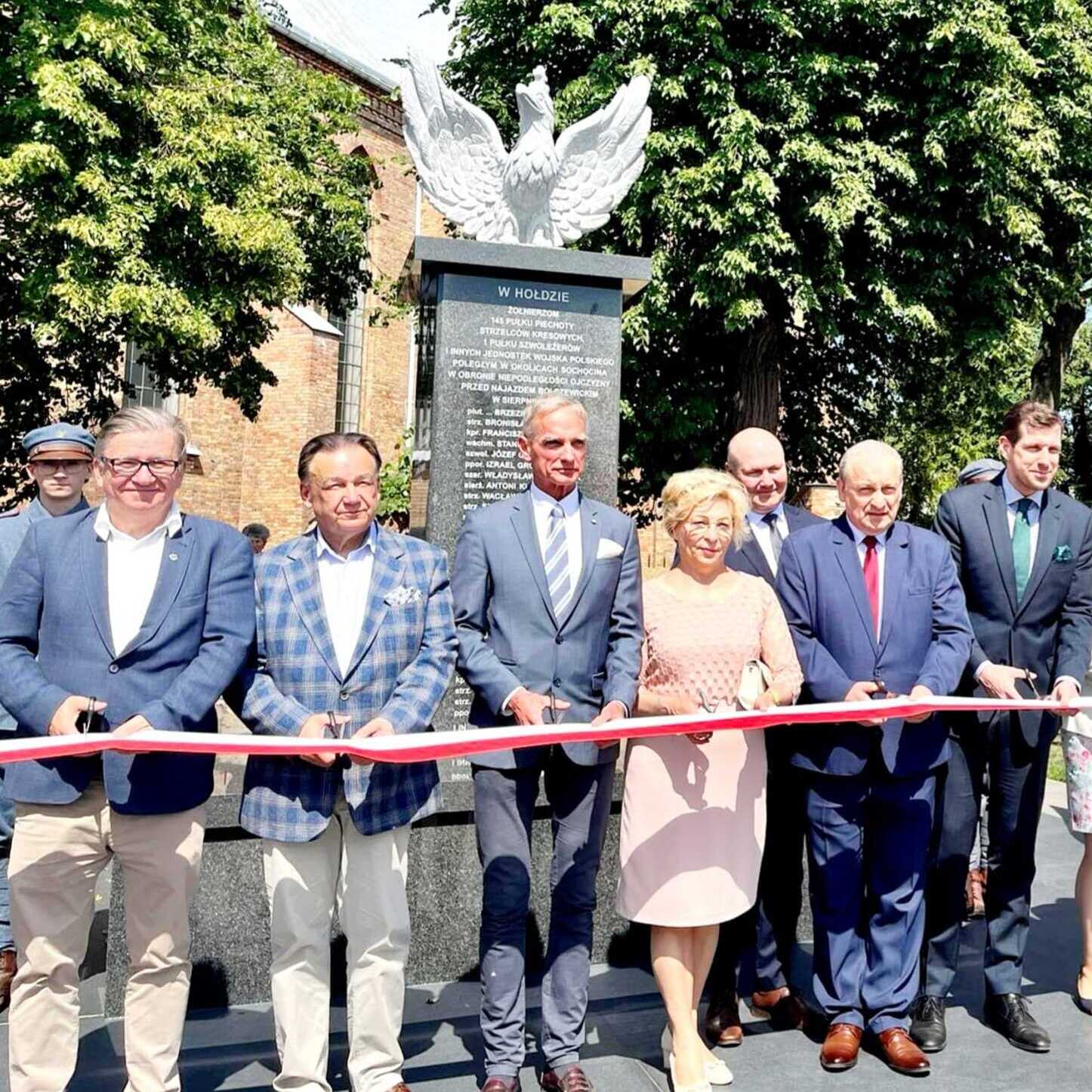 Zaproszeni goście przecinają wstęgę podczas uroczystości odsłonięcia pomnika.