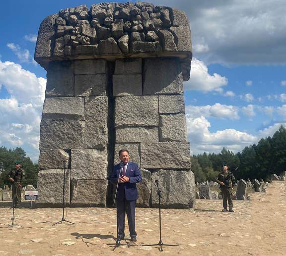 Marszałek Adam Struzik stoi przed mikrofonem na zewnątrz, na tle pomnika