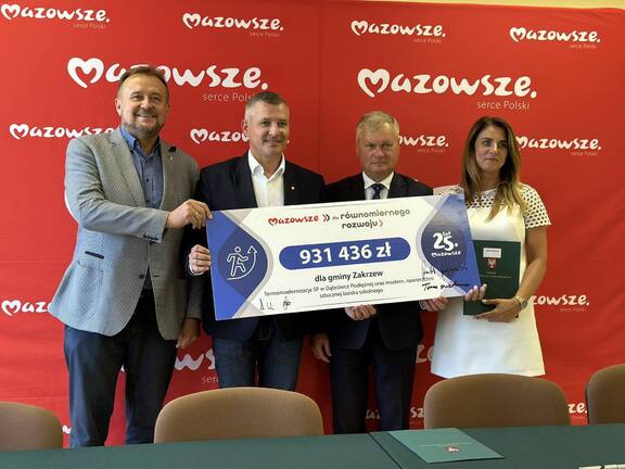 Grupa osób stoi z czekiem na tle czerwonej ścianki