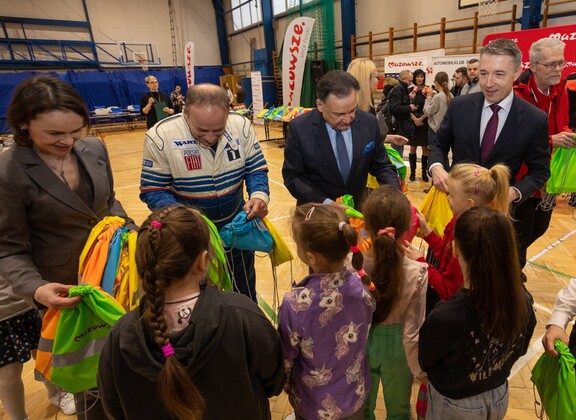 Marszałek Adam Struzik i przewodniczący Ludwik Rakowski  rozdają dzieciom plecaki z odblaskami