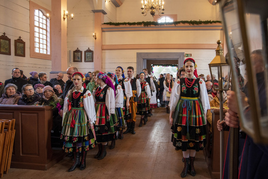 Tancerki w ludowych ubraniach stoją wzdłuż nawy kościoła